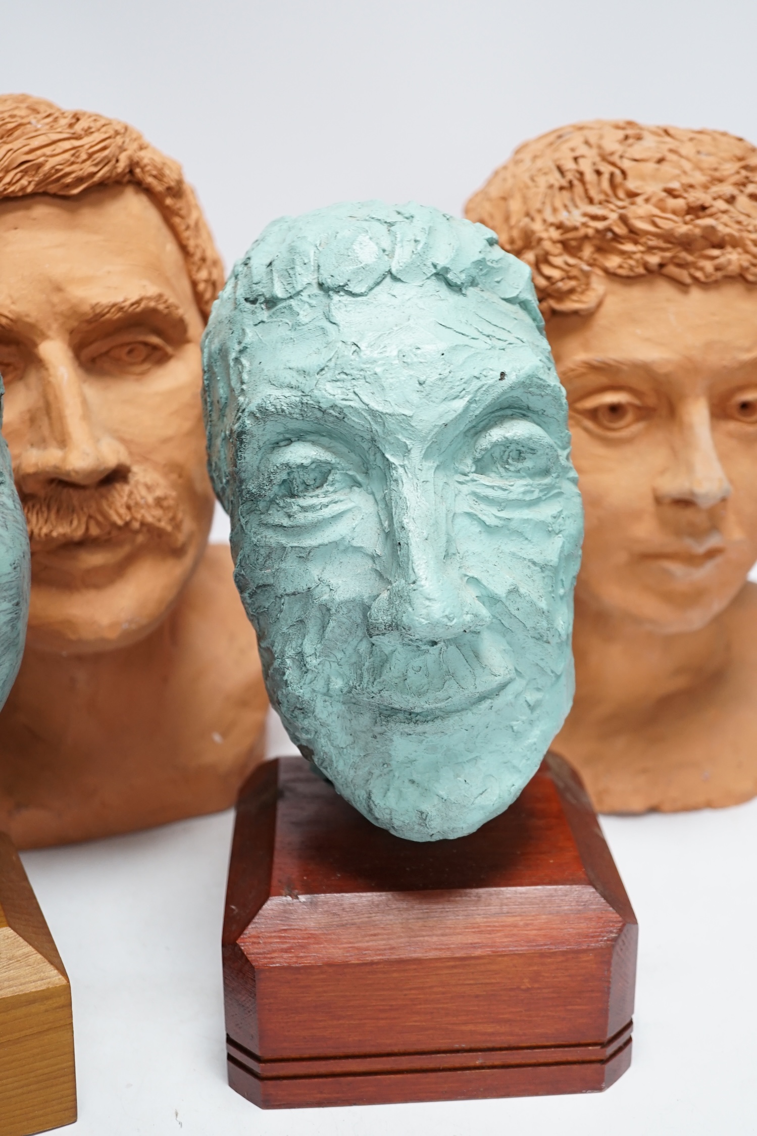 Four art pottery sculpted heads on stands, two terracotta and two painted verdigris green, largest 34cm high